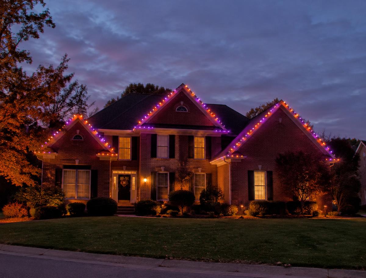 Brick home with orange and purple autumn roofline lights
